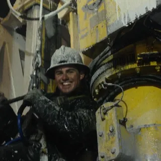 Derek Henderson on a drilling rig top drive at night, covered in frost and smiling in a hard hat.